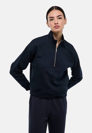 Sweatshirt bleu marine avec un col montant, fermeture éclair à moitié sur le devant, et poignets côtelés. Fabriqué en matériau doux avec une finition légèrement texturée et une coupe décontractée.