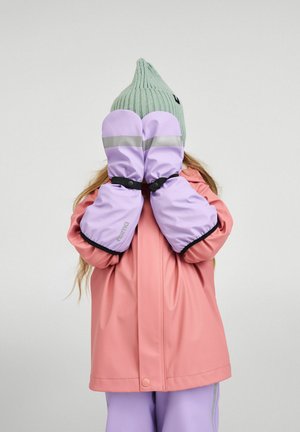 Kind trägt rosa Regenmantel, lavendelfarbene wasserdichte Fäustlinge und grüne Strickmütze, bedeckt Gesicht mit den Fäustlingen vor neutralem Hintergrund.