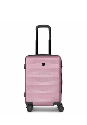 Valise rigide compacte rose poudré avec poignée télescopique et quatre roulettes noires pivotantes, vue de face sur fond blanc.
