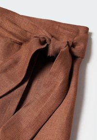 Tissu en lin marron noué en nœud papillon à la taille, mettant en valeur la texture et le détail de la fermeture.