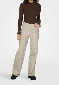 Beiget, leveälahkeiset farkut, joissa korkea vyötärö, yhdistettynä ruskeaan, pitkähihainen paita, jossa on röyhelöinen pääntie. Asussa mustat korokepohjaiset kengät.