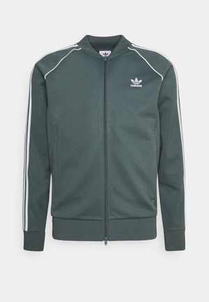 Veste zippée Adidas vert foncé avec des bandes blanches sur les manches et petit logo Adidas sur la poitrine gauche, poignets et ourlet côtelés.