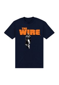 Marinblå t-shirt med "THE WIRE" i fet orange text. Centralt motiv visar en svartvit figur i lång kappa som går.