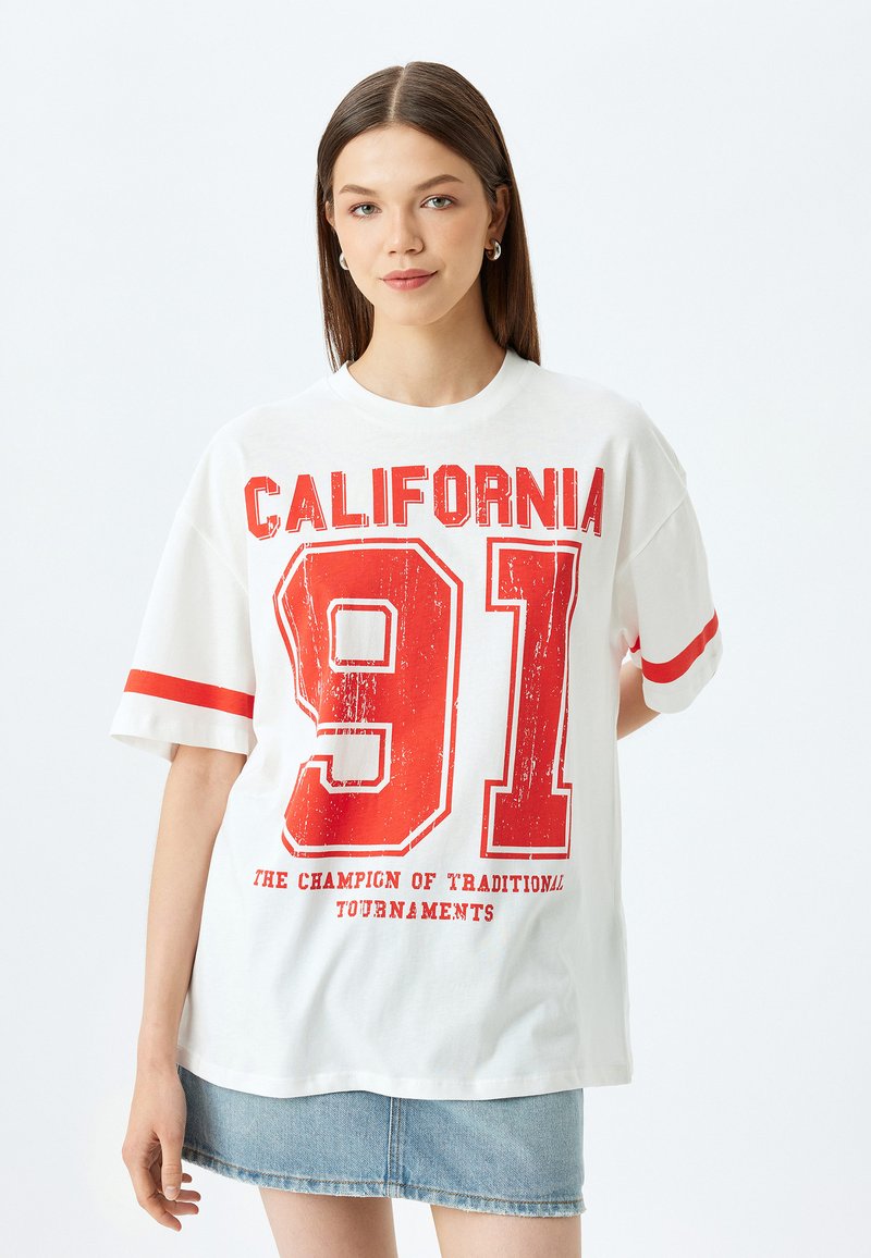 Camiseta de algodón blanca con el texto rojo "CALIFORNIA" y "91" con un efecto desgastado, mangas cortas y rayas rojas en los puños de las mangas.