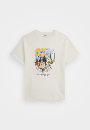 Baumwoll-T-Shirt in Creme mit kurzen Ärmeln, ausgestattet mit einem farbenfrohen Grafikdesign eines Bären in urbaner Kleidung, ergänzt durch einen Text unter der Illustration.