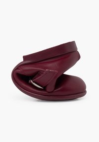 Scarpa in pelle bordeaux con design morbido e arrotondato. Presenta una struttura pieghevole e una cinghia con minuteria metallica per la chiusura.