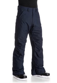 Námořnické modré zateplené sněhové kalhoty nosené s černobílými sněhovými botami, vyobrazené na osobě od pasu po nohy.
