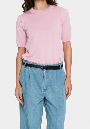 Różowy krótkim rękawem sweter z okrągłym dekoltem, zestawiony z jasnoniebieskimi dżinsami i czarnym paskiem. Gładka faktura, luźny krój.