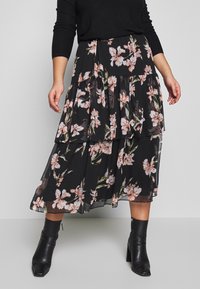 Gonna maxi nera a strati con stampa floreale in tonalità di rosa e verde, realizzata in un tessuto semitrasparente. Abbinata a stivali neri con tacco.