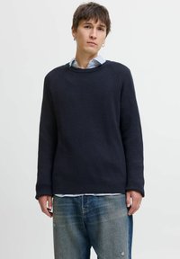 Navy ribbed knit sweater with long sleeves, round neckline, and a relaxed fit, layered over a blue and white striped shirt.