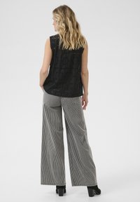 Haut sans manches noir avec un motif à œillets floraux, associé à un pantalon large à rayures gris. La tenue présente un tissu texturé et respirant.