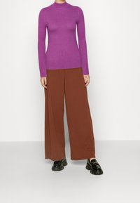 Tajta lila ribbad polotröja, matchad med vida bruna byxor. Svarta klumpiga loafers avslutar outfiten.