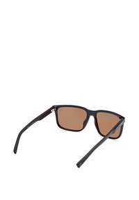 Czarne okulary przeciwsłoneczne z brązowymi soczewkami, prostokątny kształt ramki, fakturowane zauszniki i metalowe akcenty przy zawiasie.