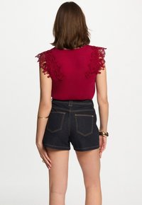 Top color marrone con dettagli in pizzo sulle spalle abbinato a pantaloni corti in denim scuro. Presenta un design aderente e accenti in hardware dorato.