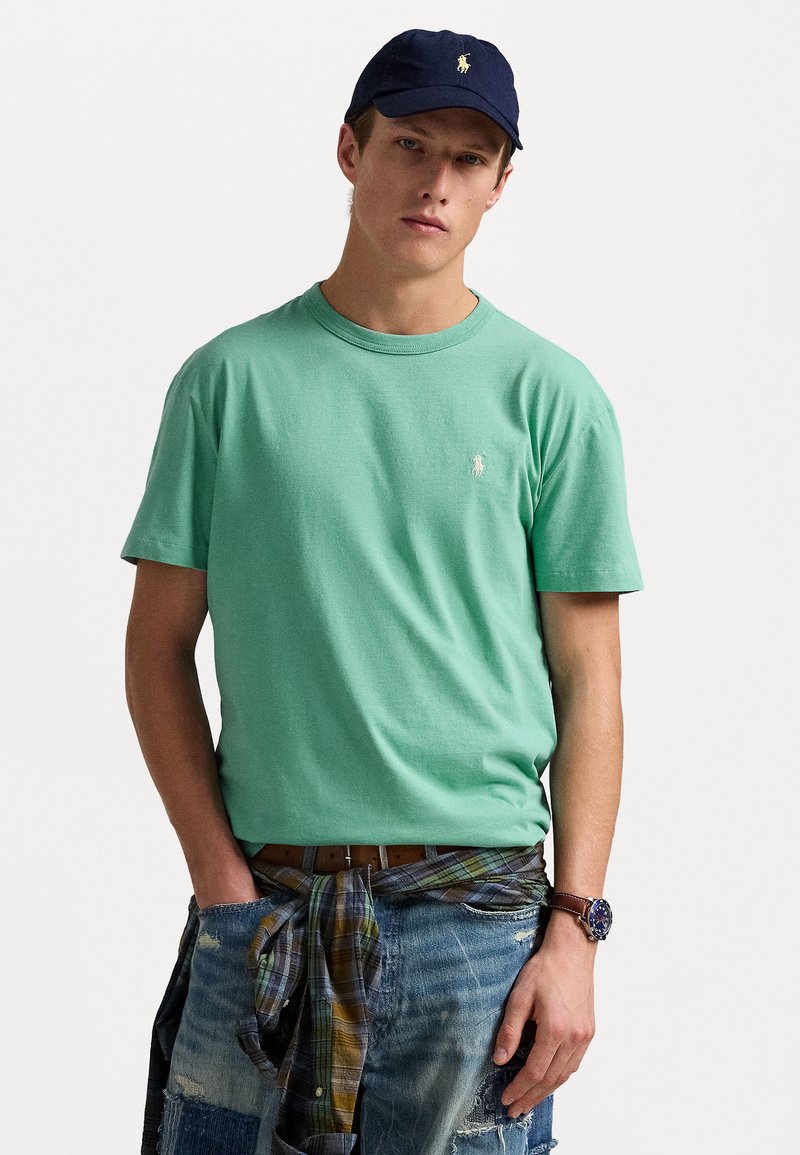 Mintgrön bomulls t-shirt med rund halsringning och broderad logotyp, tillsammans med slitna denimshorts och en rutmönstrad skjorta knuten i midjan.