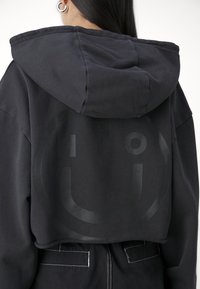 Sweat à capuche noir raccourci avec un grand motif smiley ton sur ton au dos, doté d'une capuche à cordon de serrage et d'un tissu texturé.