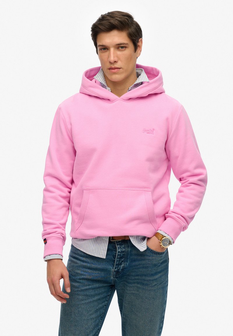 Felpa con cappuccio rosa realizzata in misto cotone. Presenta una tasca frontale, polsini a costina e un logo sul petto. Indossata sopra una maglietta a righe.