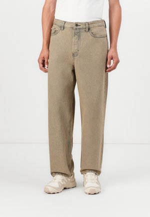 Beige high-waisted straight-leg jeans with a faded texture, five pockets, and a button closure, worn with light-colored sneakers.
