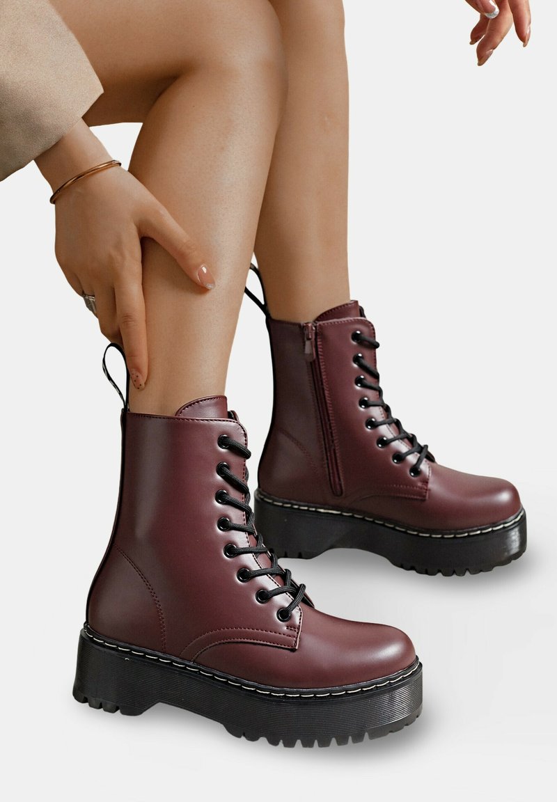 Bottines en simili cuir bordeaux avec lacets noirs, une fermeture éclair sur le côté et de grosses semelles noires avec un motif de crampons texturé.