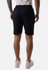 Pantaloni corti di cotone blu navy con un elastico in vita, due tasche posteriori e una superficie liscia, abbinati a sneakers bianche.