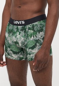 Levi's bokserice z temnim pasom, okrašene z zelenim in sivo listnatim maskirnim vzorcem, izdelane iz raztegljivega, gladkega materiala.