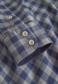 Camicia a quadre con quadrati grigio chiaro e blu navy, polsini con bottoni a contrasto e texture in morbido cotone.