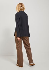 Pull bleu marine avec un ourlet côtelé et un col haut, associé à un pantalon large marron et des sandales à plateforme tan, vu de dos.