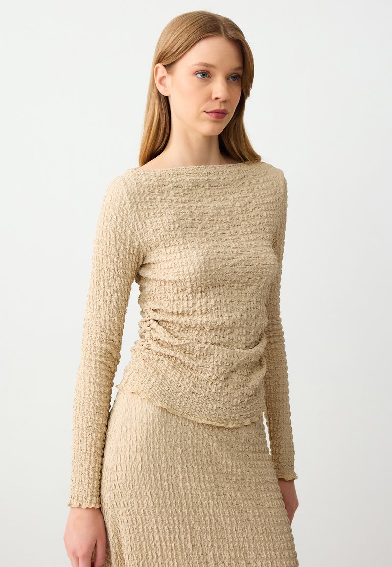 Top beige a maniche lunghe con tessuto testurizzato e stropicciato, scollatura rotonda e vestibilità slim. Progettato con un dettaglio arricciato in vita.
