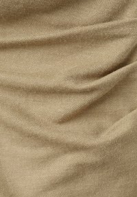 Tissu beige texturé avec un motif tissé serré, présentant des plis doux et des ombres subtiles mettant en valeur sa surface.