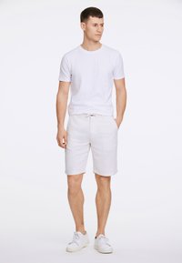 Camiseta blanca de cuello redondo combinada con pantalones cortos de lino beige claros y zapatillas blancas. Los pantalones cortos tienen bolsillos laterales y una cintura con cordón.