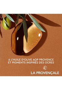 Goutte d'huile d'olive sur un fond en terre cuite texturé, accompagnée d'olives vertes et de feuilles d'olivier, avec un texte blanc en bas.