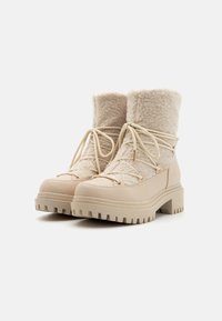 Bottes d'hiver beiges avec un dessus en laine texturée, semelle en caoutchouc et design à lacets. Comprend des éléments en métal doré et une semelle plateforme épaisse.