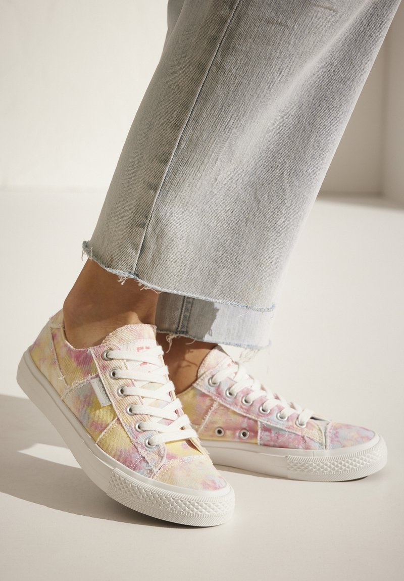 Pastel-patterned canvas sneakers with a white rubber sole, featuring lace-up design and frayed edges. Paired with slightly cropped denim jeans.