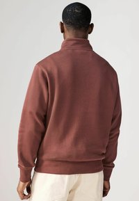 Burgundi színű pulóver magas gallérral és bordázott mandzsettákkal. Puha pamut keverék anyagból készült, laza fit és sima textúra jellemzi.