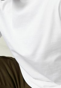 Hvid bomulds t-shirt med en glat tekstur, rund hals og korte ærmer, parret med brune stofbukser i en afslappet pasform.