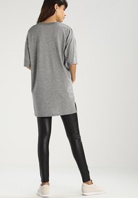 Tricou peste măsură, gri, cu mâneci scurte și deschideri laterale, asortat cu colanți negri. Modelul poartă adidași de culoare deschisă. Textură netedă.