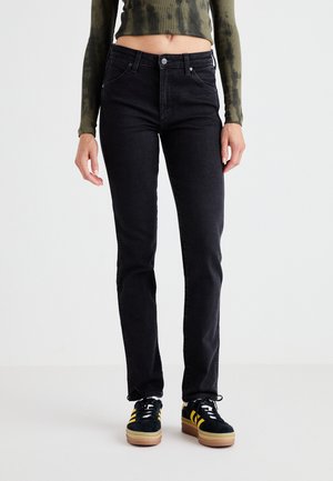 Black denim jeans with a slim fit, featuring a classic five-pocket design, metal rivets, and a subtle textured surface. Paired with dark shoes.