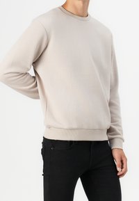 Beige mikina s kulatým výstřihem, žebrovanými manžetami a lemem. Měkká textura, volný střih, stylizována s černými upnutými džínami.