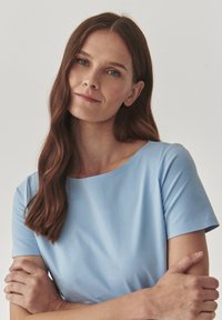 Rochie scurtă de culoare albastru deschis, cu mâneci scurte și guler rotund, cu o textură netedă și un design minimalist. Materialul pare moale și respirabil.