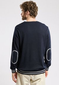 Pull marine à manches longues, avec des coudières blanches et des poignets et un ourlet à rayures côtelées. Texture lisse et coupe ajustée.