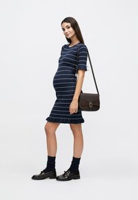 Μπλε σκούρο φόρεμα με ριγέ σχεδιασμό και κοντά μανίκια, με φουσκωτή λυγίδα. Καφέ τσάντα χιαστί, κάλτσες μέχρι το γόνατο και γυαλιστερά μαύρα μοκασίνια ολοκληρώνουν την εμφάνιση.