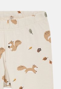 Leggings beiges avec un motif ludique d'écureuils et de glands. Ceinture élastique, texture douce, avec des feuilles dans des tons verts et bruns.