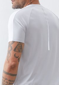 Hellgraues Sportshirt mit kurzen Ärmeln, strukturiertem Stoff und einer vertikalen Nahtdetails auf dem Rücken.
