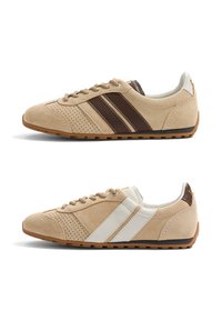 Deux paires de baskets en daim beige avec des détails perforés, des semelles en caoutchouc et des bandes latérales – une paire avec des bandes brun foncé, l'autre avec des bandes blanches.