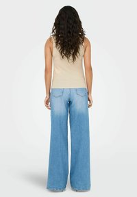 Beige geribbelde tanktop en lichtblauwe brede jeans, met een soepele textuur, hoge taille en subtiele vervaging naar de zoom toe.