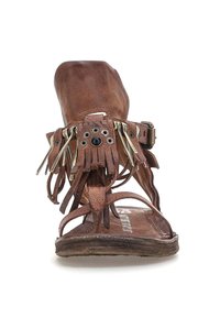 Brune lædersandal med flad sål, frynse detaljer og metal accenter. Åben tå og ankelrem design. Tekstureret fodseng synlig.