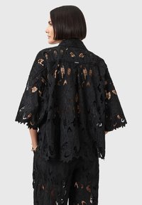 Zwarte kanten kimono met bloemmotieven, wijde mouwen en een losse pasvorm. Het ontwerp bevat sheer elementen en een kraagdetail.