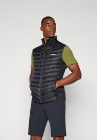 Black puffer vest with a high collar, lightweight design, and narrow horizontal stitching. Accompanied by a green short-sleeve shirt.