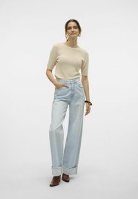 Smėlinis tekstūruotas trumpomis rankovėmis viršus, derinamas su aukštu juosmeniu, plačiomis šviesiai mėlynomis džinsomis, su sukrautais rankovėmis ir rudojo odos aukštakulniais.