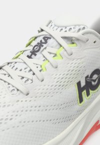 Λευκό αθλητικό παπούτσι Hoka με επάνω μέρος από δίχτυ, νεον πράσινες λεπτομέρειες, γκρι λογότυπο και λευκά κορδόνια, σε λευκό φόντο, κοντινή γωνιακή λήψη.